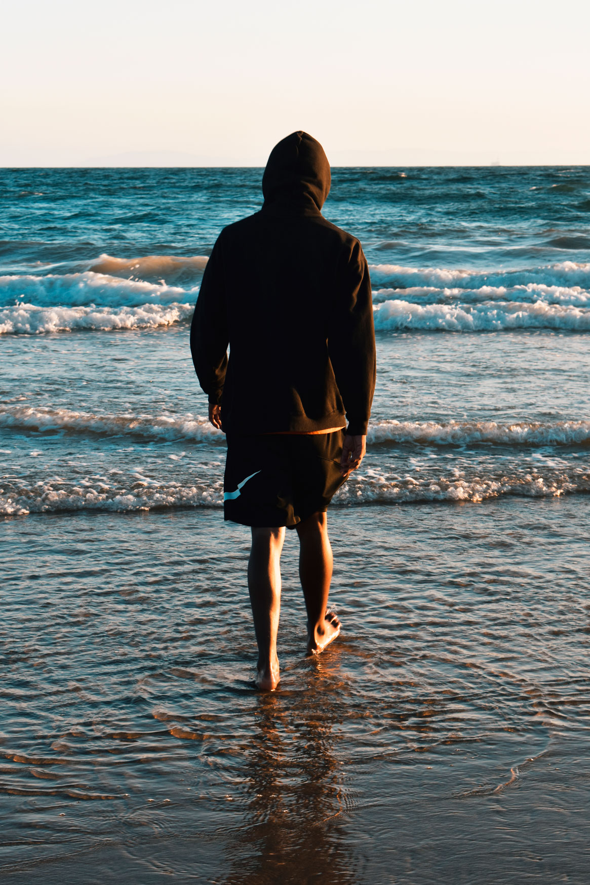 man walking into ocean with sunset